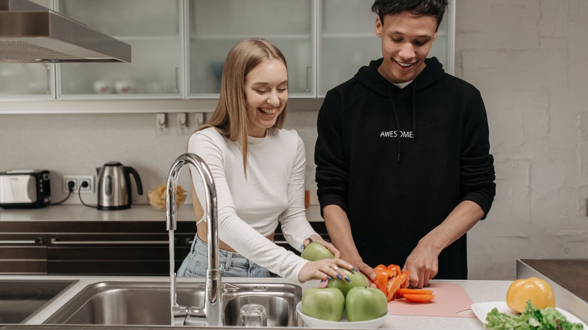 Smiling young couple cooking together in a modern kitchen, slicing fresh vegetables.